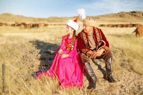 Красивая казахская пара в национальных костюмах в степи с домброй и лошадями