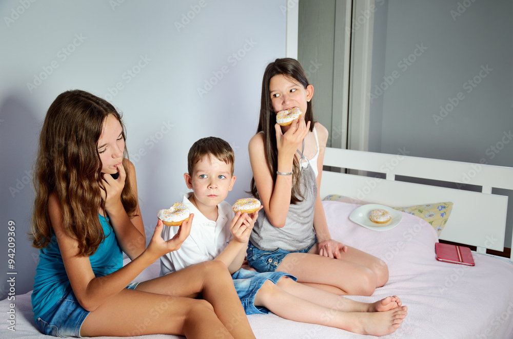 kids are sitting in bed and eating donuts