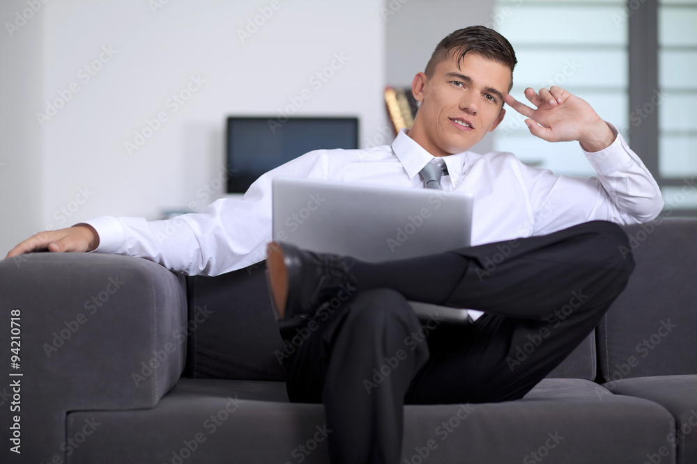 Happy young businessman looking and smiling us, sitting on couch Happy young businessman looking and smiling us, sitting on couch