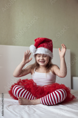 Funny girl in a Christmas cap and striped pants on the bed,