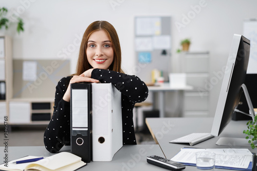 lächelnde frau im büro stützt sich auf aktenordner photo