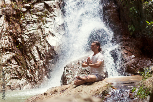 a man sits near the mountains with a beautiful waterfall