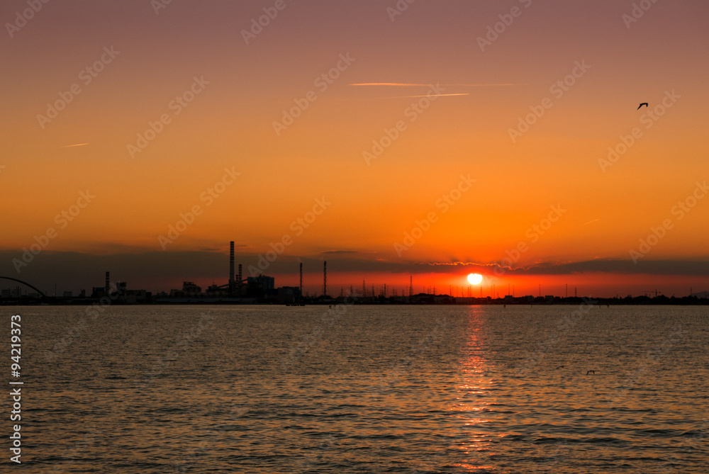 Sunset on the sea with silhouette of a chemical industrial hub.