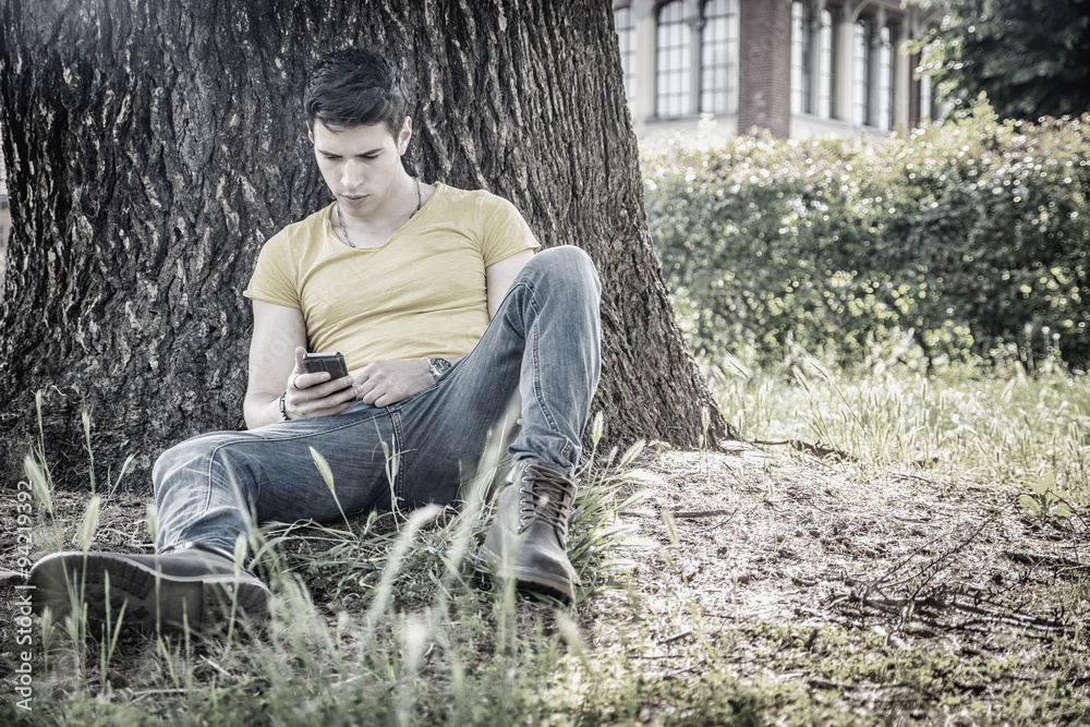Attractive young man in park resting against tree Attractive young man in park resting against tree