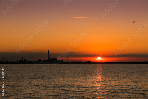 Sunset on the sea with silhouette of a chemical industrial hub. © isaac74