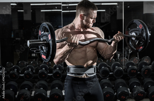 Fotografie Athlete muscular bodybuilder in the gym training biceps with bar
