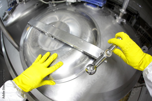 hands in yellow gloves opening industrial process tank