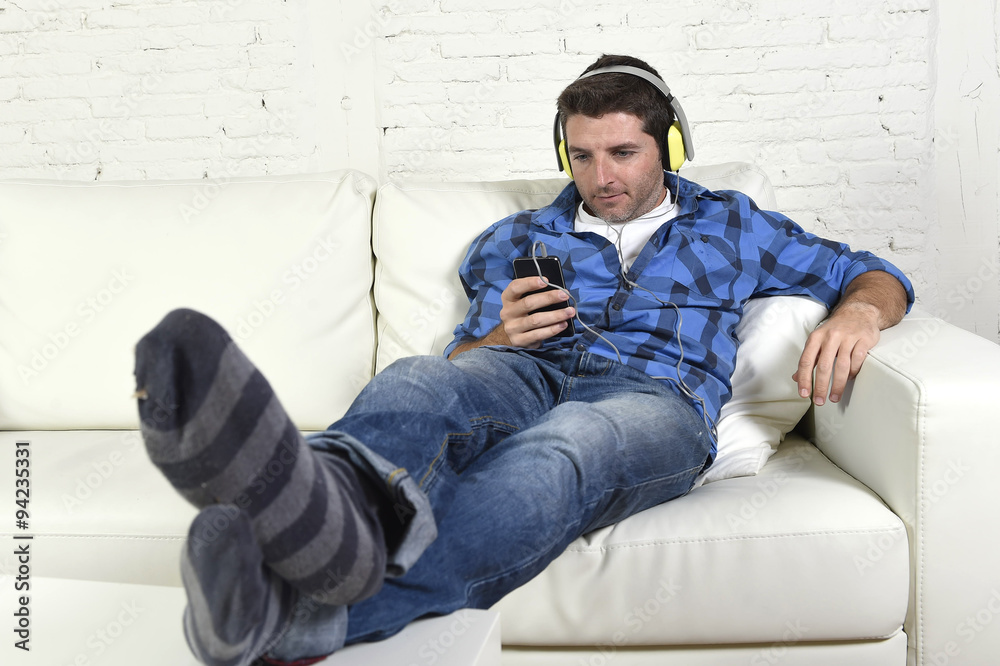 man having fun alone lying on couch listening to music with mobile phone and headphones
