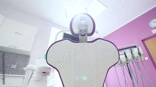 A dental clinic interior design purple dental chair with tools and dental lamp over white and purple walls, white chest of drawers and white jalousie window / camera moving right