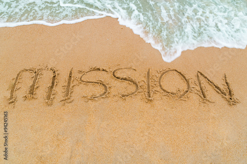MISSION inscription written on sandy beach with wave approaching