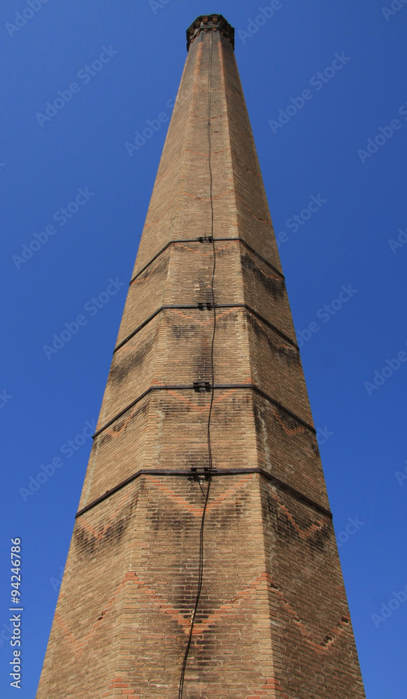 Old red brick chimney (low angle shot) with weathered brickwork against a blue sky