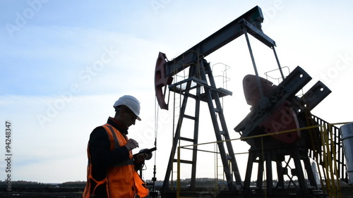 Man (Engineer, Manager, Supervisor, oilman) with tablet computer inspects the oil pumping unit. 