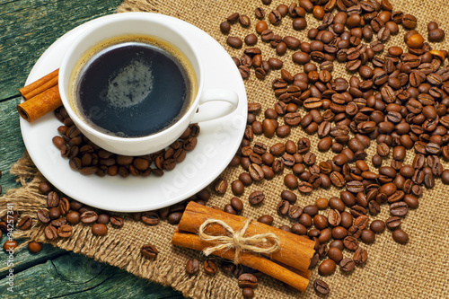 Cup of coffee, beans and cinnamon on background of jute