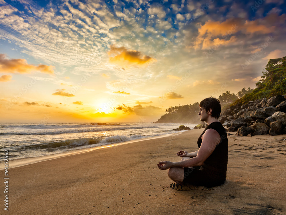 Young fit man do yoga meditation on tropical beach