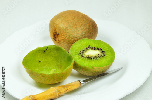 Kiwi Fruits / kiwi fruits, halved and whole, full and empty, on white plate with knife, close up, macro, horizontal  
