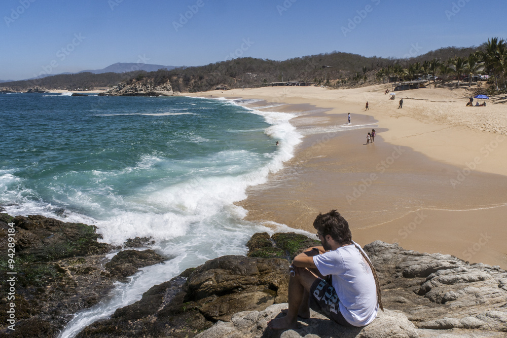 hombre joven pensando y mirando al mar sobre un risco con la playa de fondo hombre joven pensando y mirando al mar sobre un risco con la playa de fondo