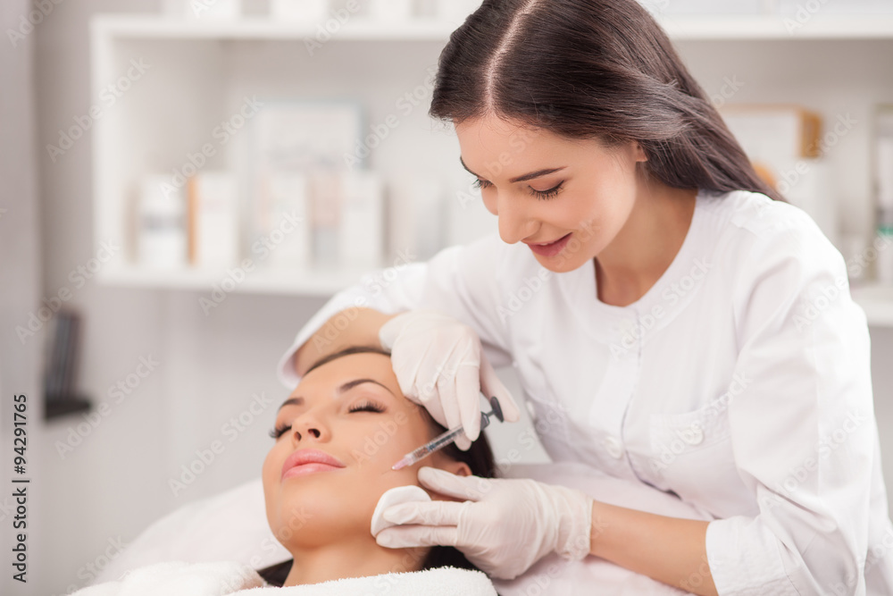 Attractive expert beautician is injecting female face