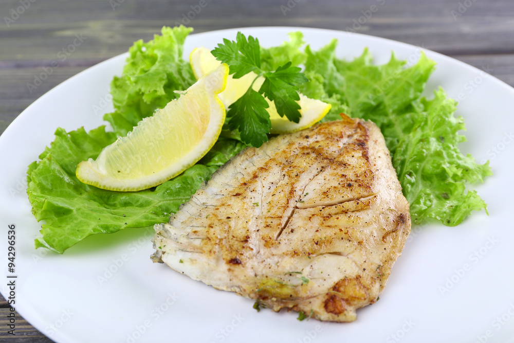Dish of fish fillet with lettuce and lemon on table close up