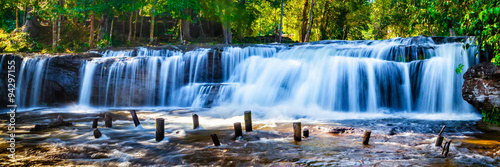 Fototapeta Wodospad z niebieską wodą wśród słonecznych lasów XXL