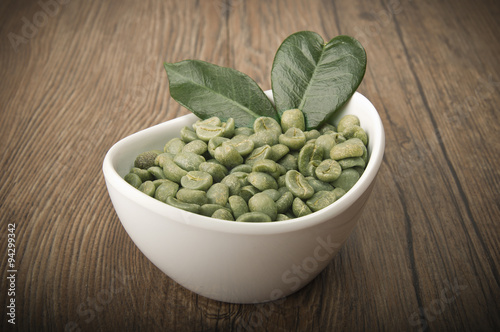 White bowl with green coffee beans on the wood