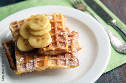 Sweet homemade waffles with sliced banana on plate, on light background