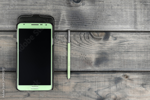 On the wooden table is a smartphone and stylus green