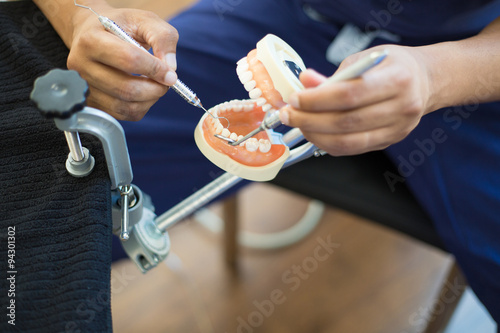 Closeup portrait, young oral professional student practicing dental procedures on plastic teeth, wax typodont mounted on table. Drilling cavity preparations and filling with restorative materials photo