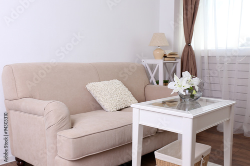 Pastel color sofa with beautiful pillows and vase with flowers on the table in front of it in the room