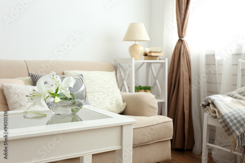 Pastel color sofa with beautiful pillows and vase with flowers on the table in front of it in the room