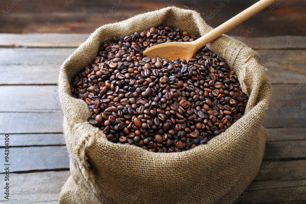 Sac with roasted coffee beans with spoon on wooden background