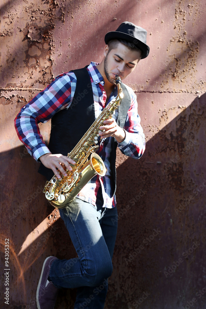 Handsome young man plays sax on old brown wall background