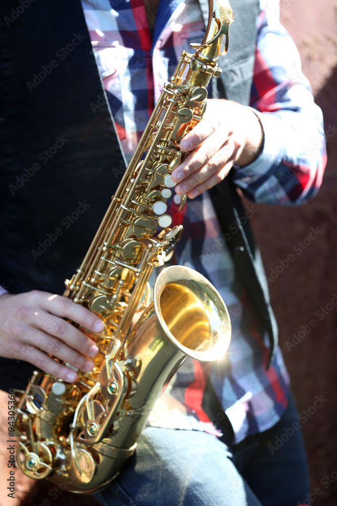Obraz premium Handsome young man with sax on old brown wall background, close up