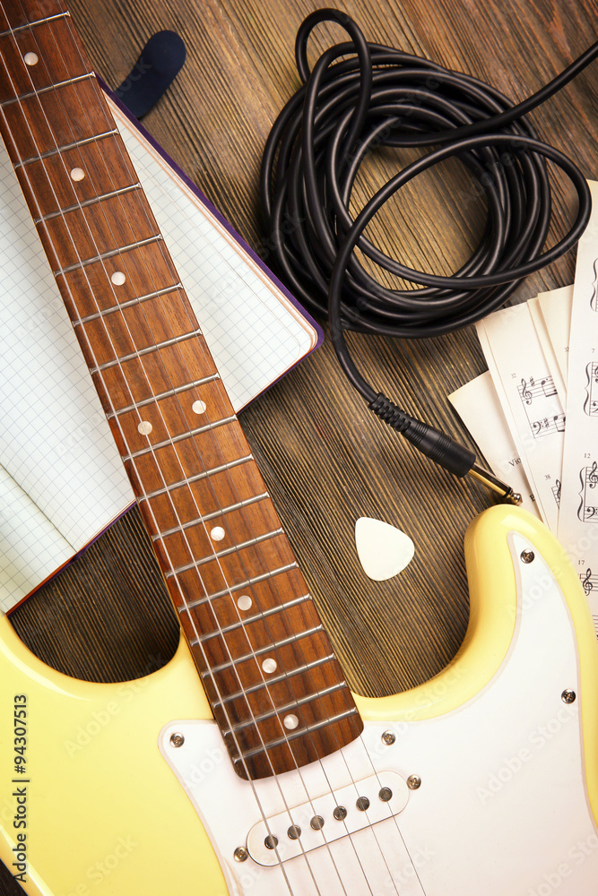 Naklejka premium Electric guitar with musical notes and cord on wooden background