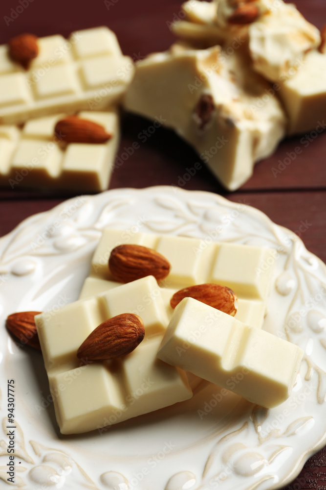White chocolate pieces with nuts on plate, on color wooden background White chocolate pieces with nuts on plate, on color wooden background