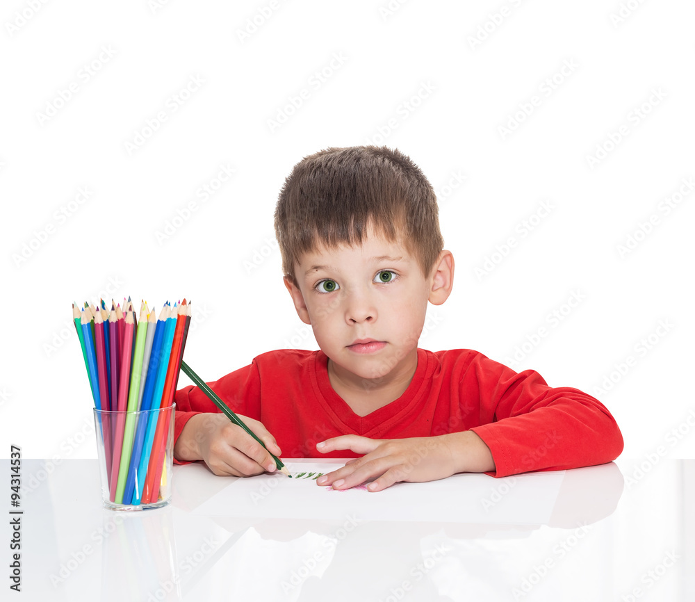 The five-year-old boy sits at a white table and draws pencils, isolated on a white background The five-year-old boy sits at a white table and draws pencils, isolated on a white background