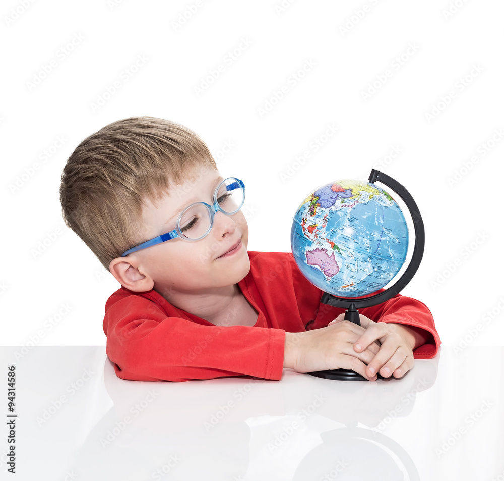 The five-year-old boy in blue points sits at a white table and holds the globe in hand, isolated on a white background The five-year-old boy in blue points sits at a white table and holds the globe in hand, isolated on a white background