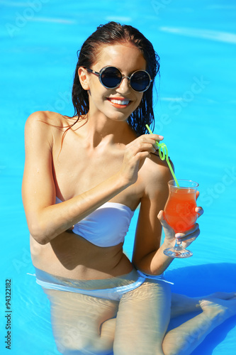 Young woman enjoying cocktail in swimming pool at summertime