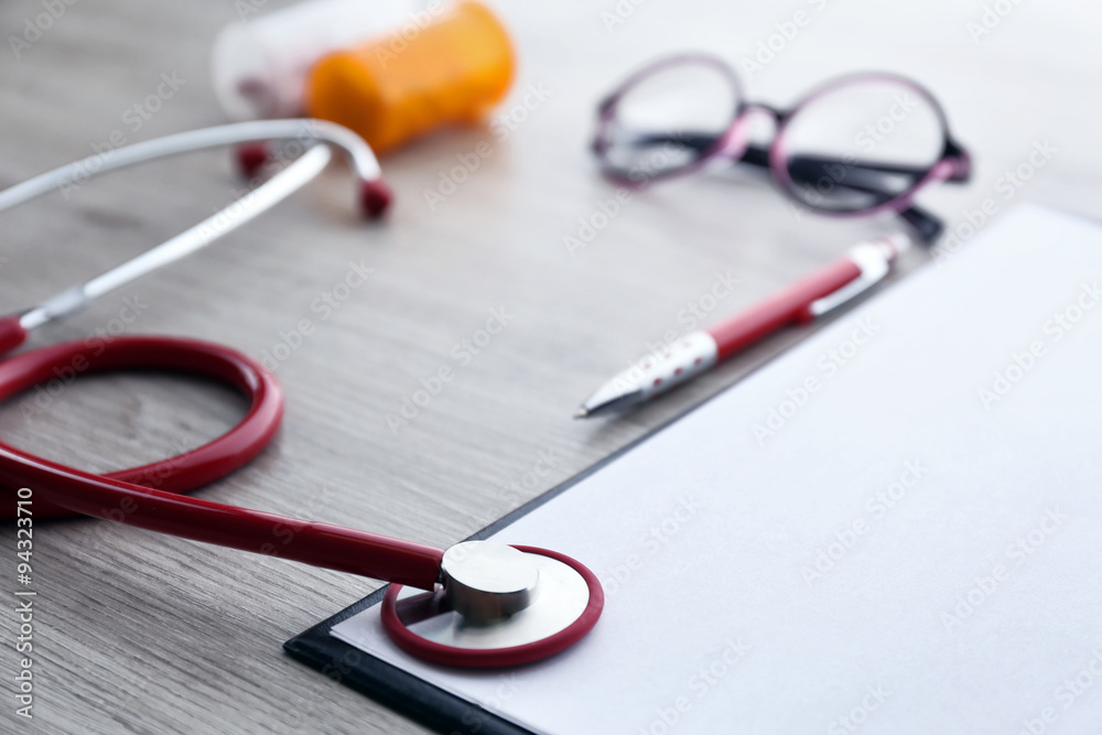 Medical stethoscope with clipboard and pills on wooden table close up Medical stethoscope with clipboard and pills on wooden table close up