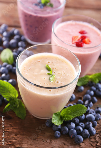 Tasty blueberry, strawberry and milk yogurts with berries and mint around on wooden background
