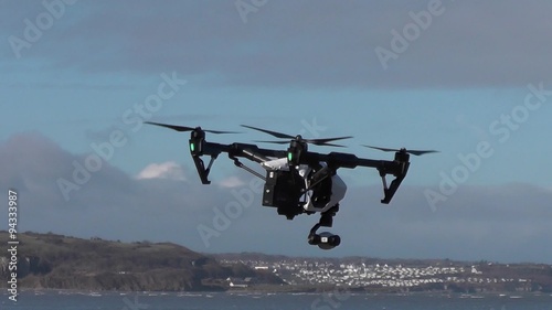 Small camera drone rotates to face the viewer and then flies out of frame.