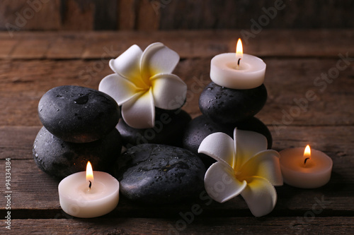 Relaxing composition with exotic fragipani flower, pebbles and candles on wooden background