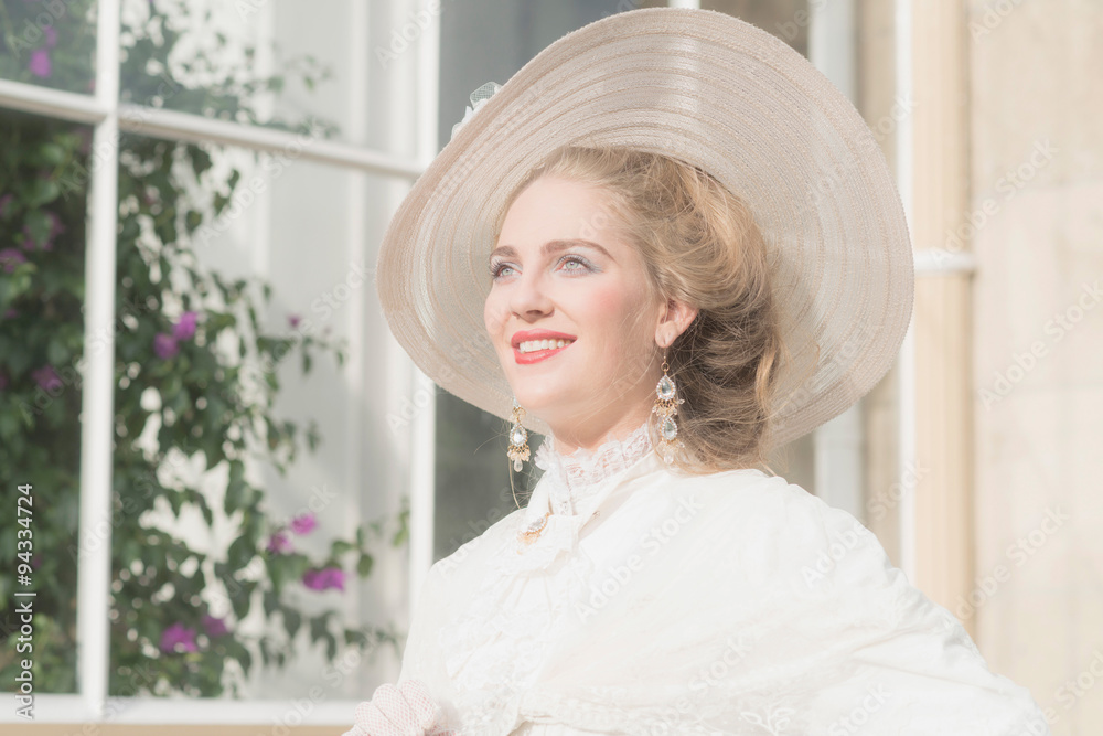 Smiling chic victorian woman with hat in front of window. Smiling chic victorian woman with hat in front of window.