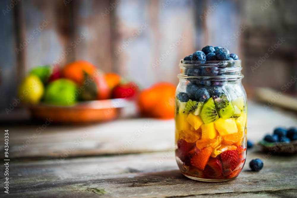 Colorful fruit salad in a jar on rustic wooden background