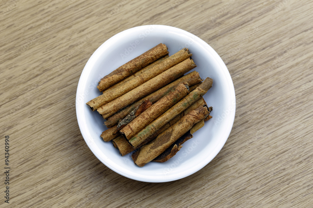 Dry cinnamon sticks in white bowl on wooden table Dry cinnamon sticks in white bowl on wooden table
