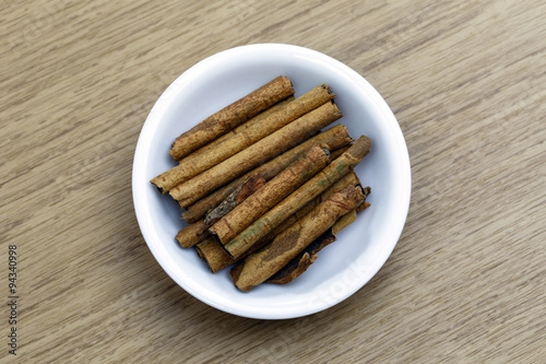 Dry cinnamon sticks in white bowl on wooden table