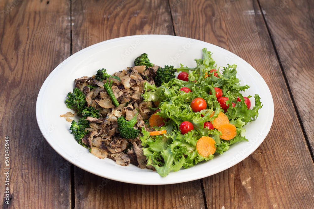 Warm mushroom salad on white plate and wooden background Warm mushroom salad on white plate and wooden background