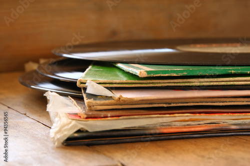 selective focus of records stack with record on top over wooden table. vintage filtered 