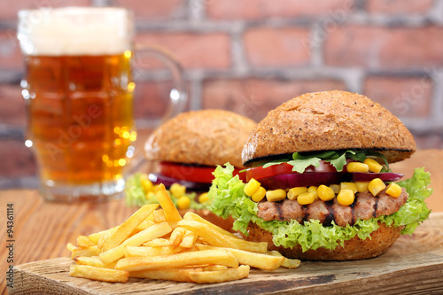 Grilled hamburger with fries and beer on brick wall background