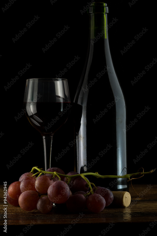 Uva rossa con bicchiere e bottiglia di vino sfondo nero su tavolo antico, tavolo legno vecchio