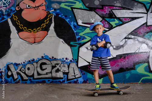 Confident small skateboarder in front of graffiti